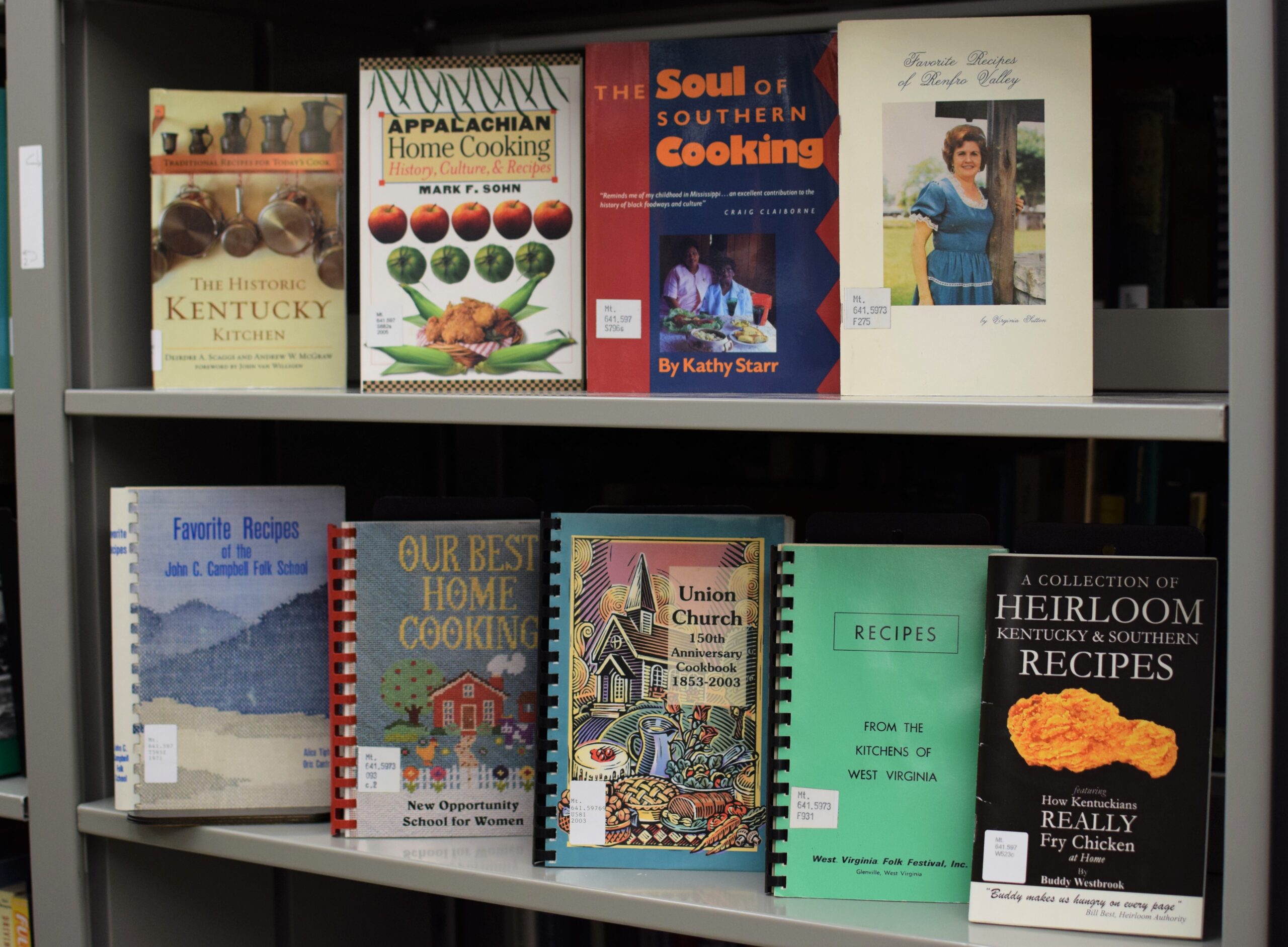 Photograph featuring 9 differing cookbooks on metal shelving in a library collection.